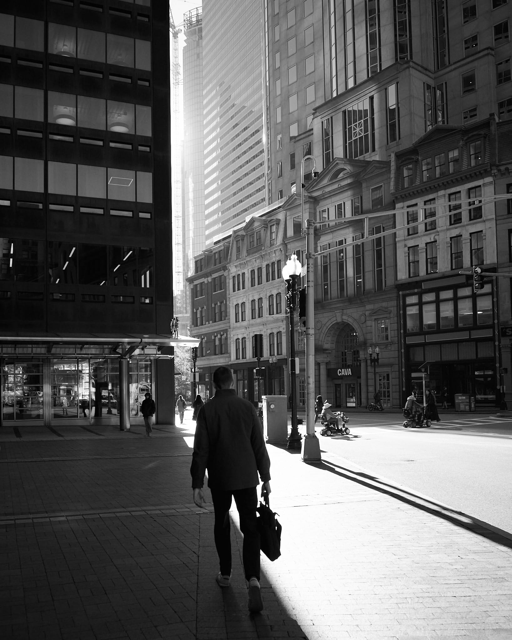 A black and white photo of a man with a briefcase walking into a bright ray of light cutting between skyscrapers